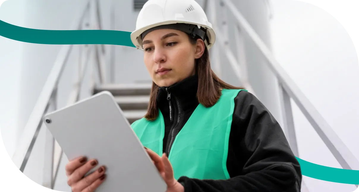 Engenheira de segurança com capacete e colete verde consultando um tablet em uma escada industrial