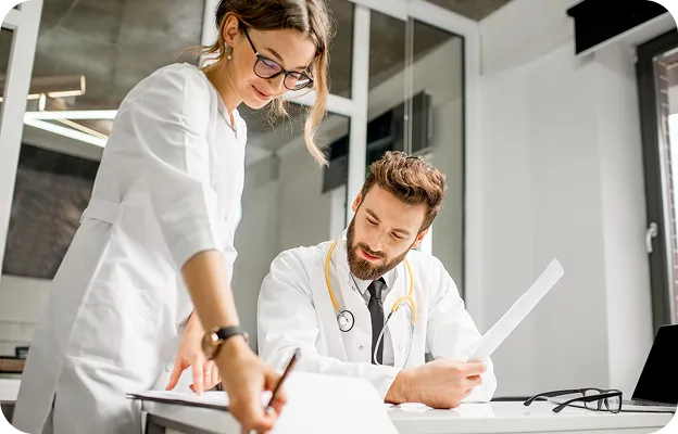 Médica e médico analisando documentos juntos em um consultório