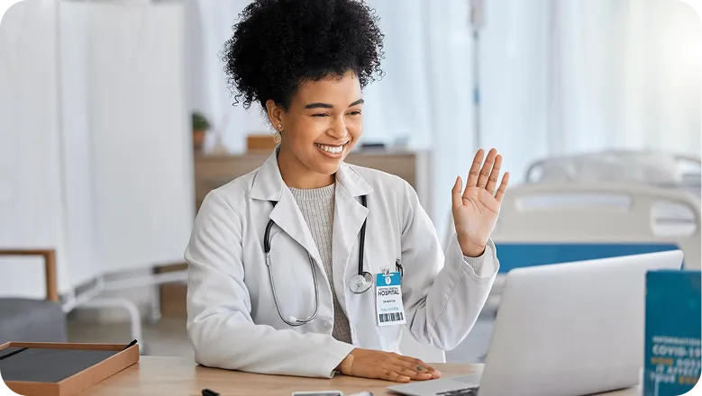 Médica sorrindo e acenando em uma videochamada no notebook